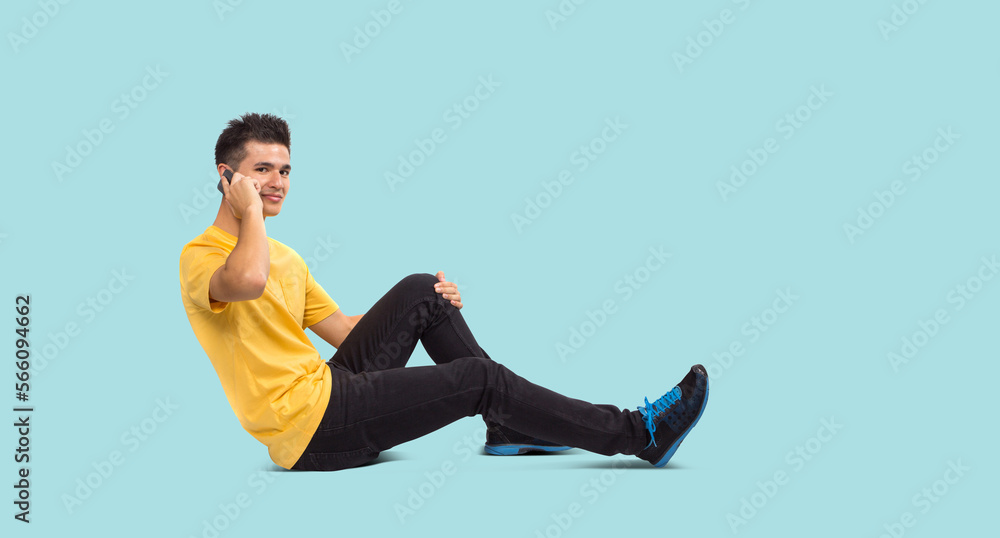 Full body Teenage boy portrait sitting using smart phone, isolated on blue background