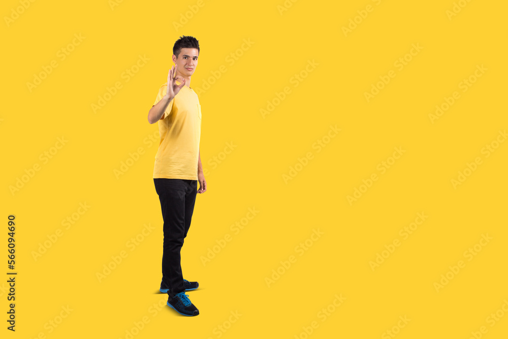 Full body Teenage boy portrait wearing casual t-shirt showing sign of ok, isolated on yellow background Full body Teenage boy portrait wearing casual t-shirt showing sign of ok, isolated on yellow background
