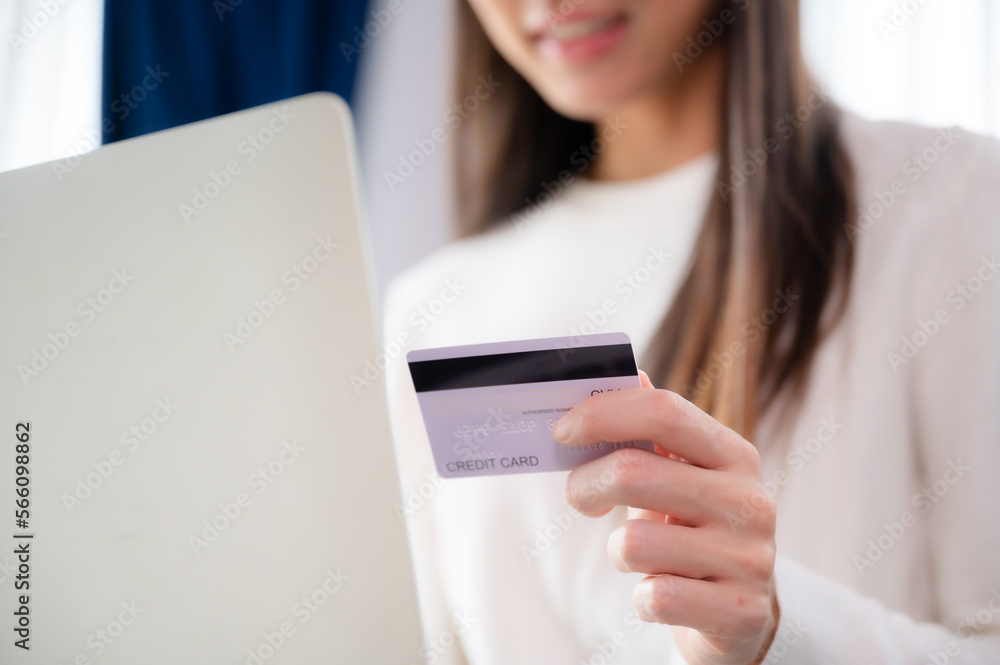 Young asian woman sitting on sofa in living room, makes online banking payments through the internet from bank card on computer laptop. Shopping online on notebook with credit card Young asian woman sitting on sofa in living room, makes online banking payments through the internet from bank card on computer laptop. Shopping online on notebook with credit card