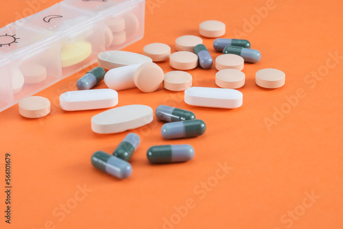 Various colors and sizes of pills are on the orange background. Selective focus on the magenta-colored pill standing at the center