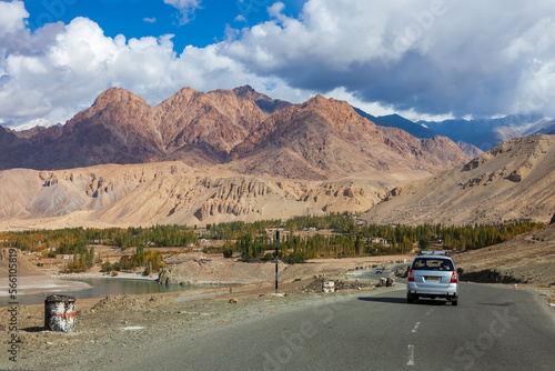Rural road in north India with a mountain backdrop in winter. High mountains and cedar forests change color in rural winter travel. Leh Ladakh countryside of India. © Issara