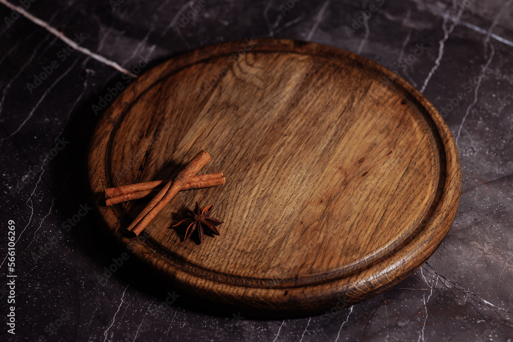 A round wooden tray with a dark finish sits on a dark background resembling marble. The minimalistic design of the tray against the sleek background creates a stylish and sophisticated look.