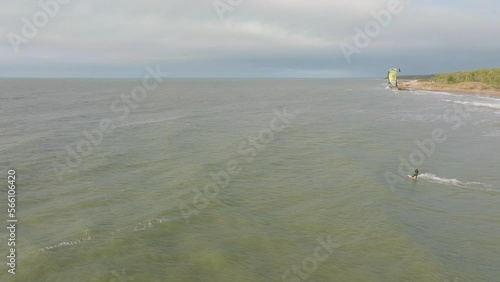 Establishing aerial view of a group of people engaged in kitesurfing, overcast winter day, high waves, extreme sport, Baltic Sea Karosta beach (Liepaja), wide drone shot moving forward