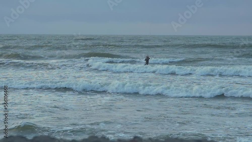 Man engaged in kitesurfing, overcast winter day, high waves, Baltic Sea Karosta beach (Liepaja), slow motion, distant shot