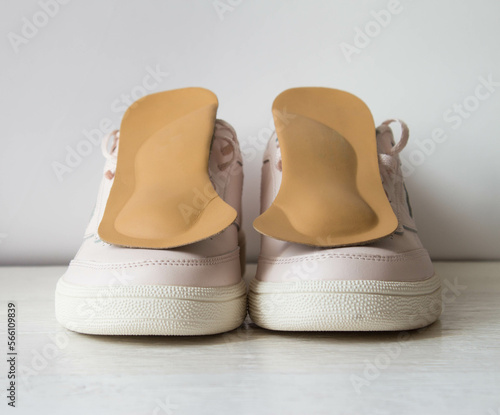 Leather orthopedic insoles with pink sports shoes isolated on white wooden board. Foot care conception.