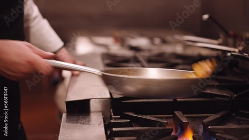 Cook shakes the silver pan with pasta back and forth while the pasta cooks on the fire. Close up dolley shot photo