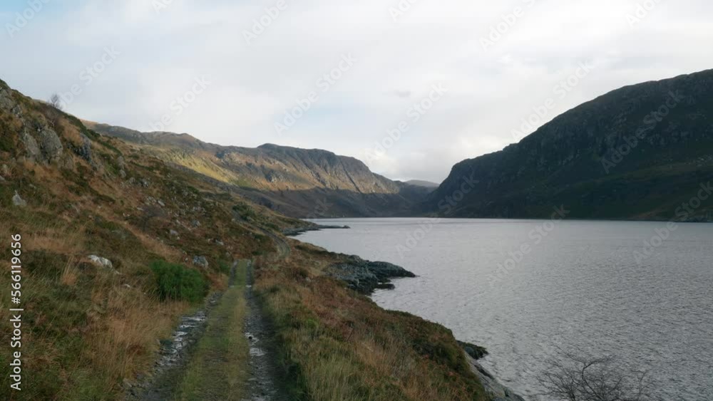 Looking down a remote hiking trail, sunlight highlights the distant mountain slopes of a dark Scottish glen filled with a large sea loch and surrounded by tall cliffs. Loch Gleann Dubh, Scotland. Looking down a remote hiking trail, sunlight highlights the distant mountain slopes of a dark Scottish glen filled with a large sea loch and surrounded by tall cliffs. Loch Gleann Dubh, Scotland.