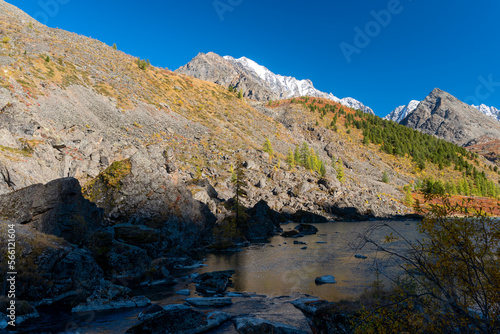 Part of an alpine lake near the stone shores in the shade against the backdrop of the mountains in Altai.
