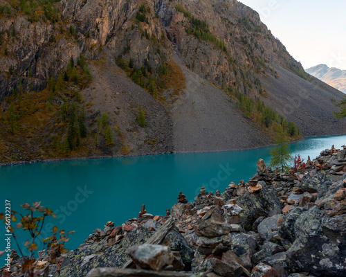 The stones laid out on top of each other stand on a rocky shore against the backdrop of a mountain and a high-altitude clean turquoise lake Shavlinskoye in Altai. photo