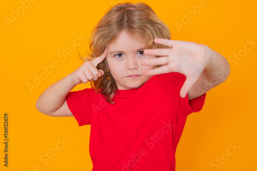 Child in red t-shirt making stop gesture on isolated studio background. Kid showing warning symbol, hand sign no. Kids protection, bullying, abuse and violence concept.