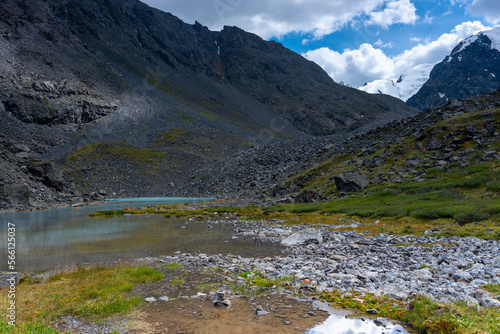 Mountain lake with clear water Karakabak in the Altai mountains with snowy peaks and glaciers with under the clouds and green grass.