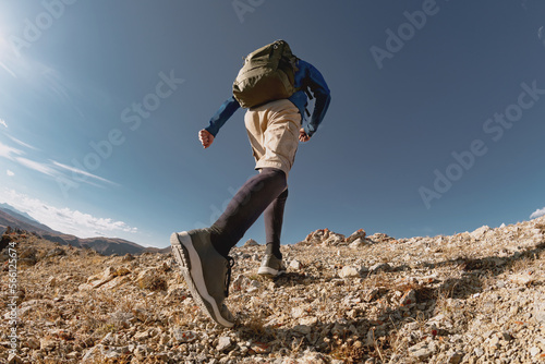 Sporty man walk with backpack uphill in mountains. Close up photo from bottom view