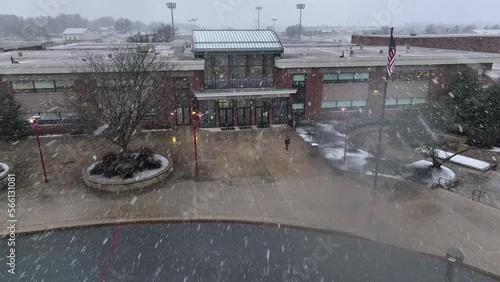 Aerial approach towards student walking out of American school building during snow storm. Snow on drone camera lens. Early dismissal. photo