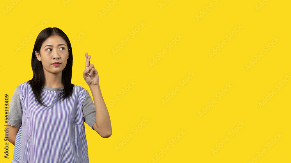 Young Asian woman making a symbolic gesture with fingers crossed showing good luck, White lie gesture, Fingers crossed, Woman doing hand sign on yellow background, Superstitious concept. Young Asian woman making a symbolic gesture with fingers crossed showing good luck, White lie gesture, Fingers crossed, Woman doing hand sign on yellow background, Superstitious concept.