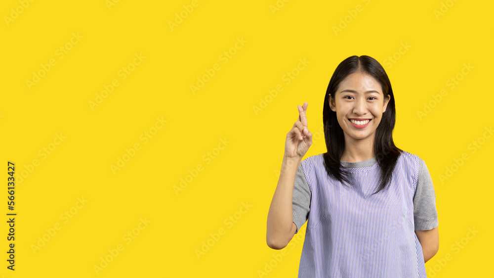 Young Asian woman making a symbolic gesture with fingers crossed showing good luck, White lie gesture, Fingers crossed, Woman doing hand sign on yellow background, Superstitious concept. Young Asian woman making a symbolic gesture with fingers crossed showing good luck, White lie gesture, Fingers crossed, Woman doing hand sign on yellow background, Superstitious concept.