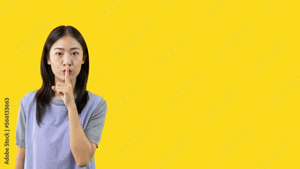 Asian woman doing silent gesture with finger, Noiseless symbol, Noisy mall, Hide a secret, Do not speak. shut your mouth, Noiseless signal transmission, Isolated on yellow background. Asian woman doing silent gesture with finger, Noiseless symbol, Noisy mall, Hide a secret, Do not speak. shut your mouth, Noiseless signal transmission, Isolated on yellow background.