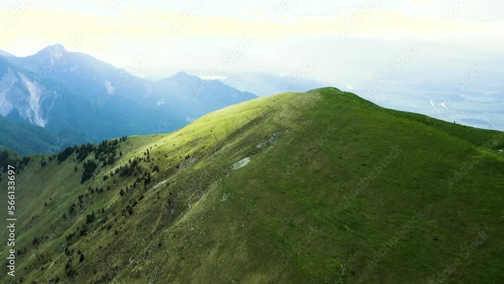 Aerial Shot of Epic Warm Lit Naked Golica Hill That Lies in Range of Western Karawanks, Next to The Austrian Border With Rare Forest Standing on Slope of the Hill. Blue Mountains, Hills in Backround. Aerial Shot of Epic Warm Lit Naked Golica Hill That Lies in Range of Western Karawanks, Next to The Austrian Border With Rare Forest Standing on Slope of the Hill. Blue Mountains, Hills in Backround.