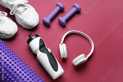 Sports water bottle with equipment, headphones and sneakers on red background