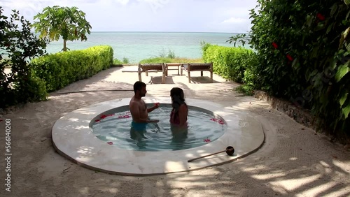 Man placing a red flower on the ear of his wife and kissing inside a pool with views to the beach in Kiwengwa, Zanzibar