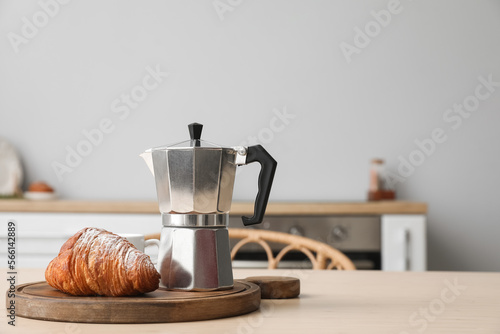 Board with geyser coffee maker and croissant on table in kitchen photo