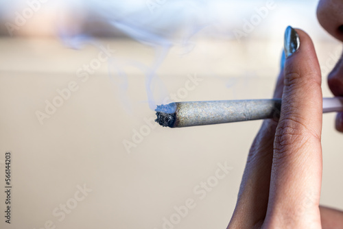 Lady holding a lit joint with smoking blowing out