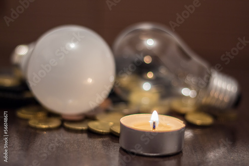 A burning candle and light bulbs near a wallet with money. Blackouts and rising electricity prices due to the war in Ukraine