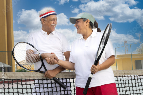 Older couple shaking hands on tennis court. © G-images