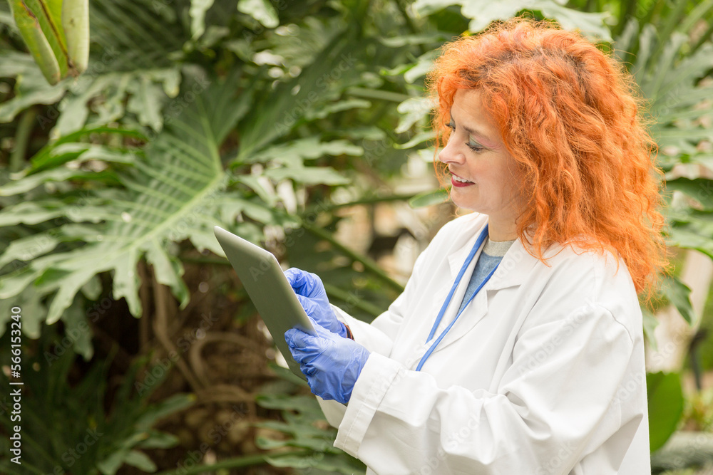 Woman in a lab coat using a tablet in a greenhouse