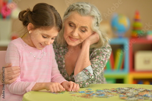 Grandmother with little granddaughter collecting puzzle at home
