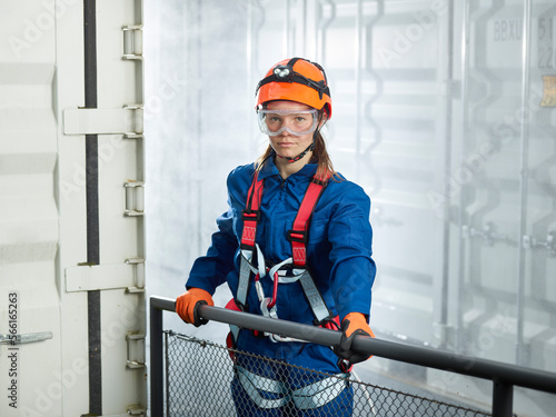 Female worker in climbing harness standing by cargo container, portrait