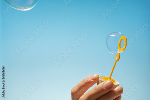 Close up side view shot of young man blowing soap bubbles on blue background. Focus on hands and wand.  © Tetiana