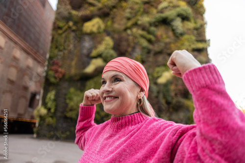 Smiling mature woman in pink sweater flexing muscles