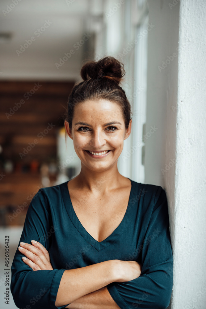 Smiling freelancer with arms crossed leaning on wall at home office Smiling freelancer with arms crossed leaning on wall at home office