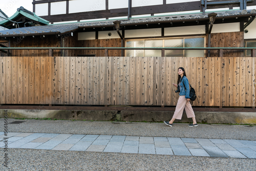 full length horizontal banner of leisure asian woman traveler walking along wooden fence wall at the exterior of Japanese traditional house in uji neighborhood in Kyoto japan full length horizontal banner of leisure asian woman traveler walking along wooden fence wall at the exterior of Japanese traditional house in uji neighborhood in Kyoto japan