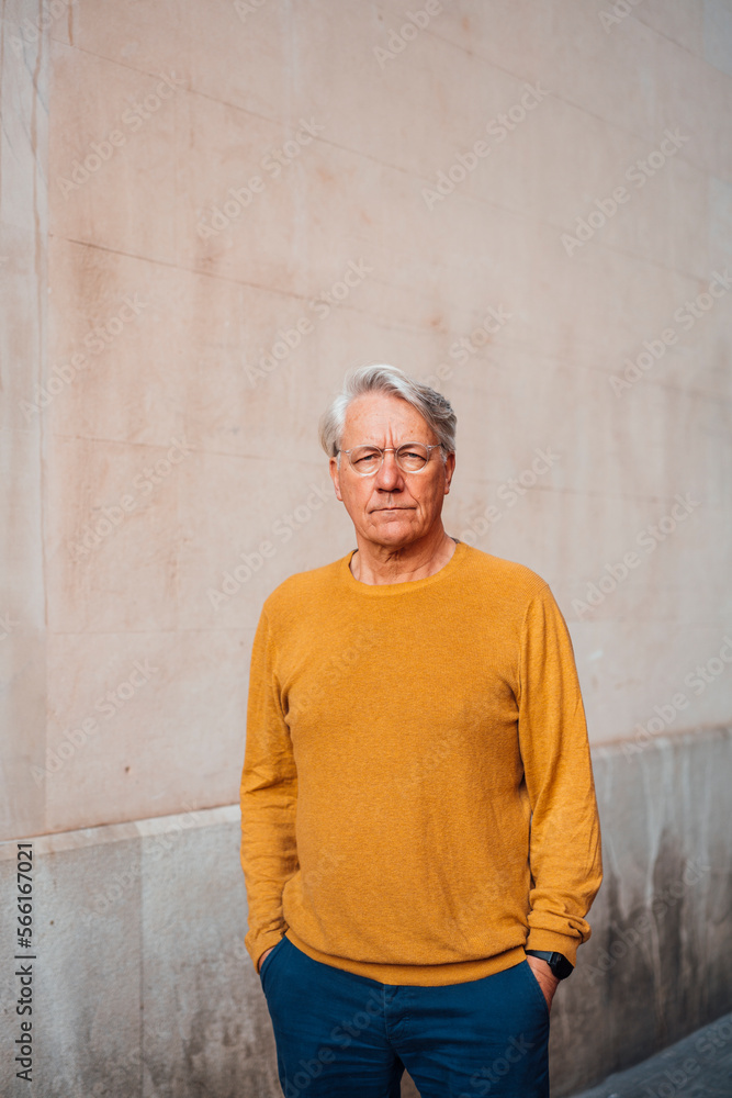 Senior man standing with hands in pockets in front of wall Senior man standing with hands in pockets in front of wall