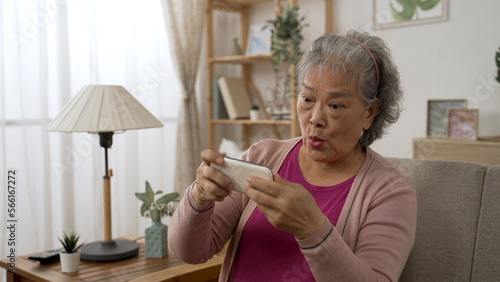 cheerful asian Japanese grey haired grandma is playing an exciting racing game on the mobile phone in the living room at home.