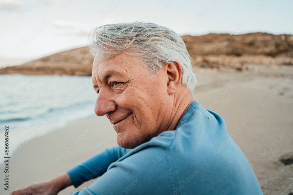 Smiling senior man sitting on beach at sunset Smiling senior man sitting on beach at sunset