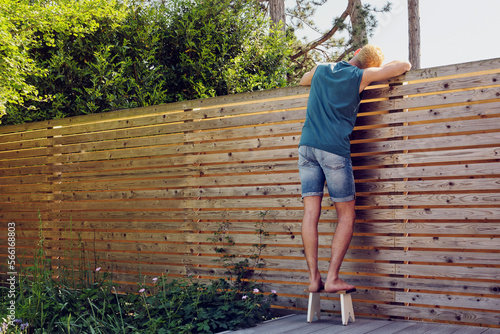 Young man looking over wooden fence at back yard photo