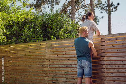 Happy man carrying woman looking over wooden fence at back yard
