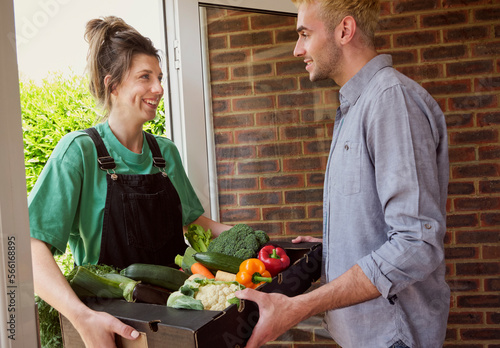 Customer receiving fresh vegetables from delivery person standing at doorway