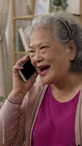 Vertical Screen: happy asian grandmother is smiling while enjoying chatting with friend on the mobile phone in a modern bright living room at home