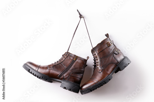 A pair of brown colored leather boots hanging on a white background.