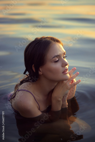 Beautiful young woman in lake water in summer dress at sunset. Portrait of a romantic wet girl at sunset, warm sun, natural beauty of a woman