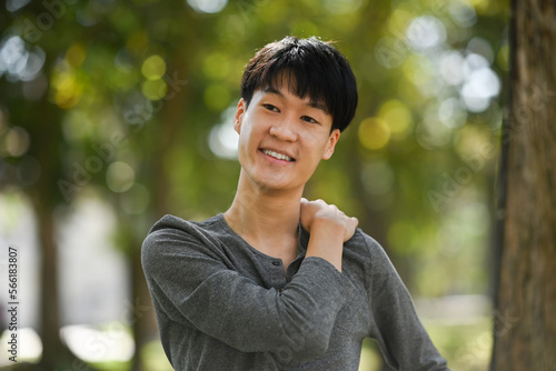 Pleasant asian man in casual clothes relaxing, stretching arms while standing in the park outdoors