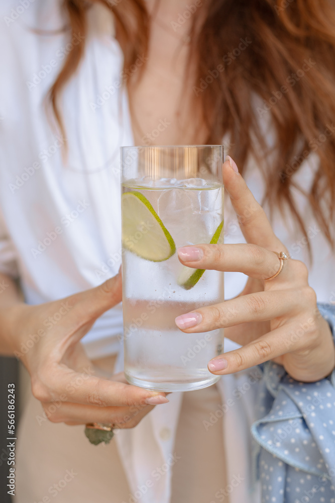 Glass of sparkling water or gin tonik with slices of lime held by a woman Glass of sparkling water or gin tonik with slices of lime held by a woman