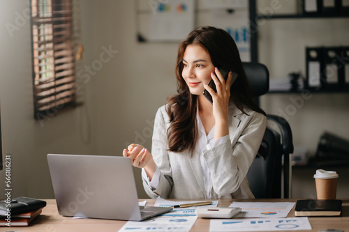 Business asian woman Talking on the phone and using a laptop with a smile while sitting at office..