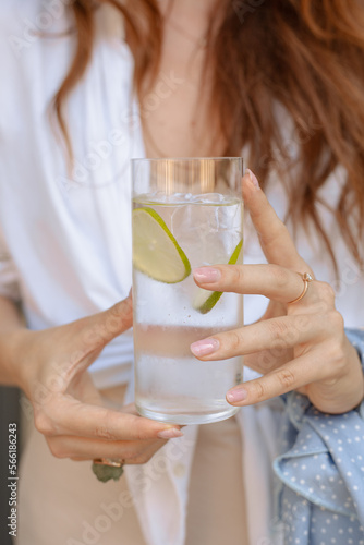 Glass of sparkling water or gin tonik with slices of lime held by a woman