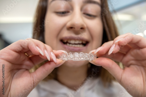 Portrait of beautiful girl patient holding orthodontic retainers aligners in dental clinic.