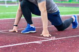 Close-up of the male hands of an athlete with smartwatches at a low start, the man prepared for a marathon race. Training process of a sprinter athlete at a stadium with a rubber coating