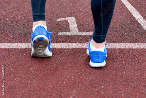 Runner prepares for a marathon race in the track, number one. Close-up of the foot of an athlete in blue sneakers kneading his feet before a race on track number one. 